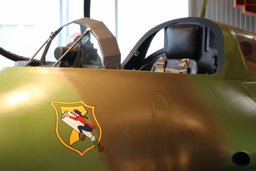 The bullet proof glass in the cockpit of the Me 163B and the 7 Staffel (squadron) of JG 400 emblem showing Baron Münchhausen flying skyward on an uncorked champagne bottle 